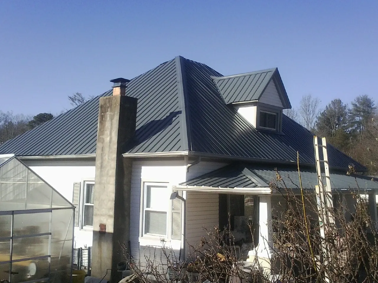 Dark blue standing seam metal roof on a white farmhouse with dormer — Slate & Tile Roof Repair by Roofing Brothers in Okemos