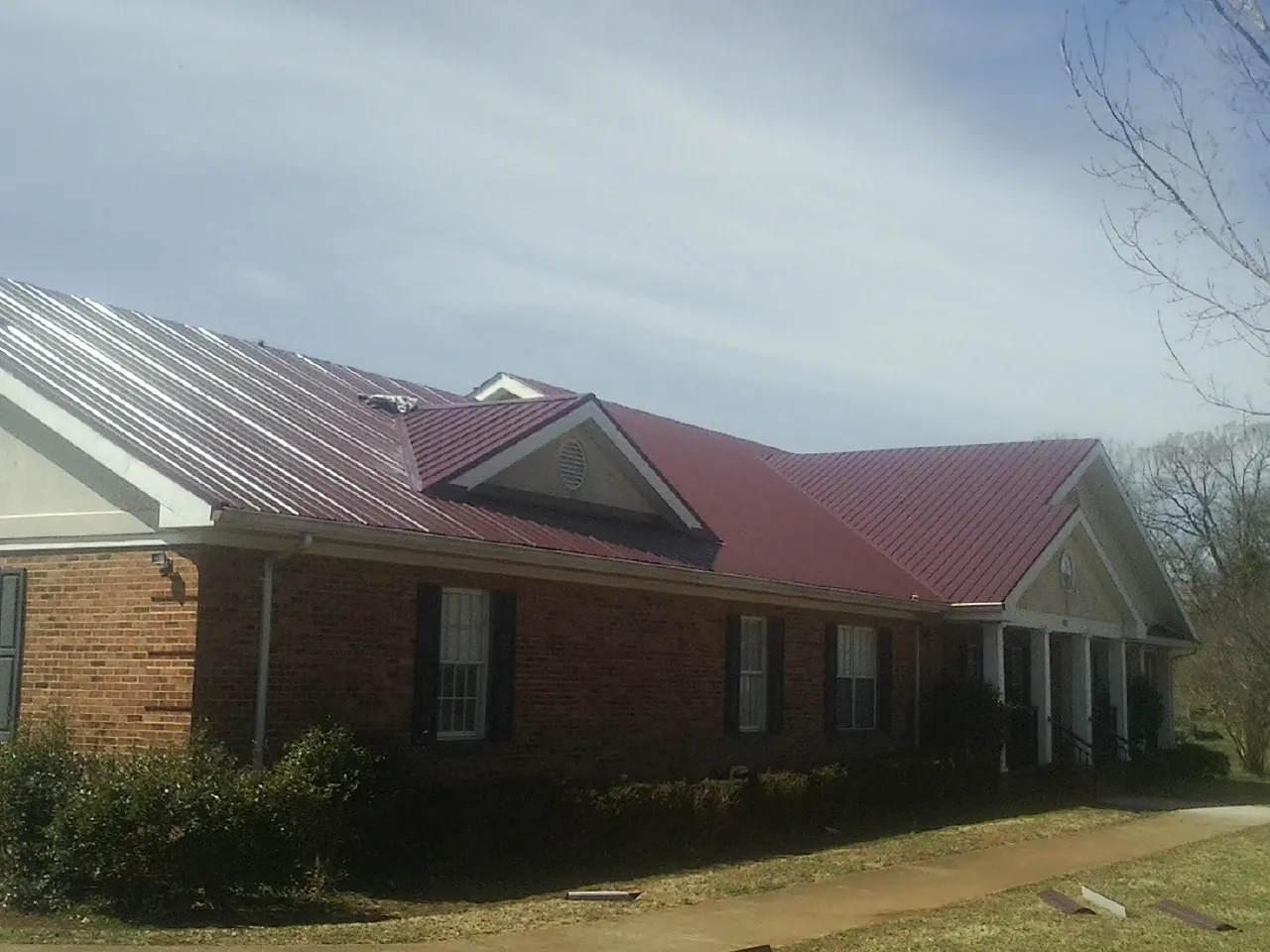 Red metal roof with gabled entries on a long brick building, from a Hail Damage Roof Repair job in Okemos