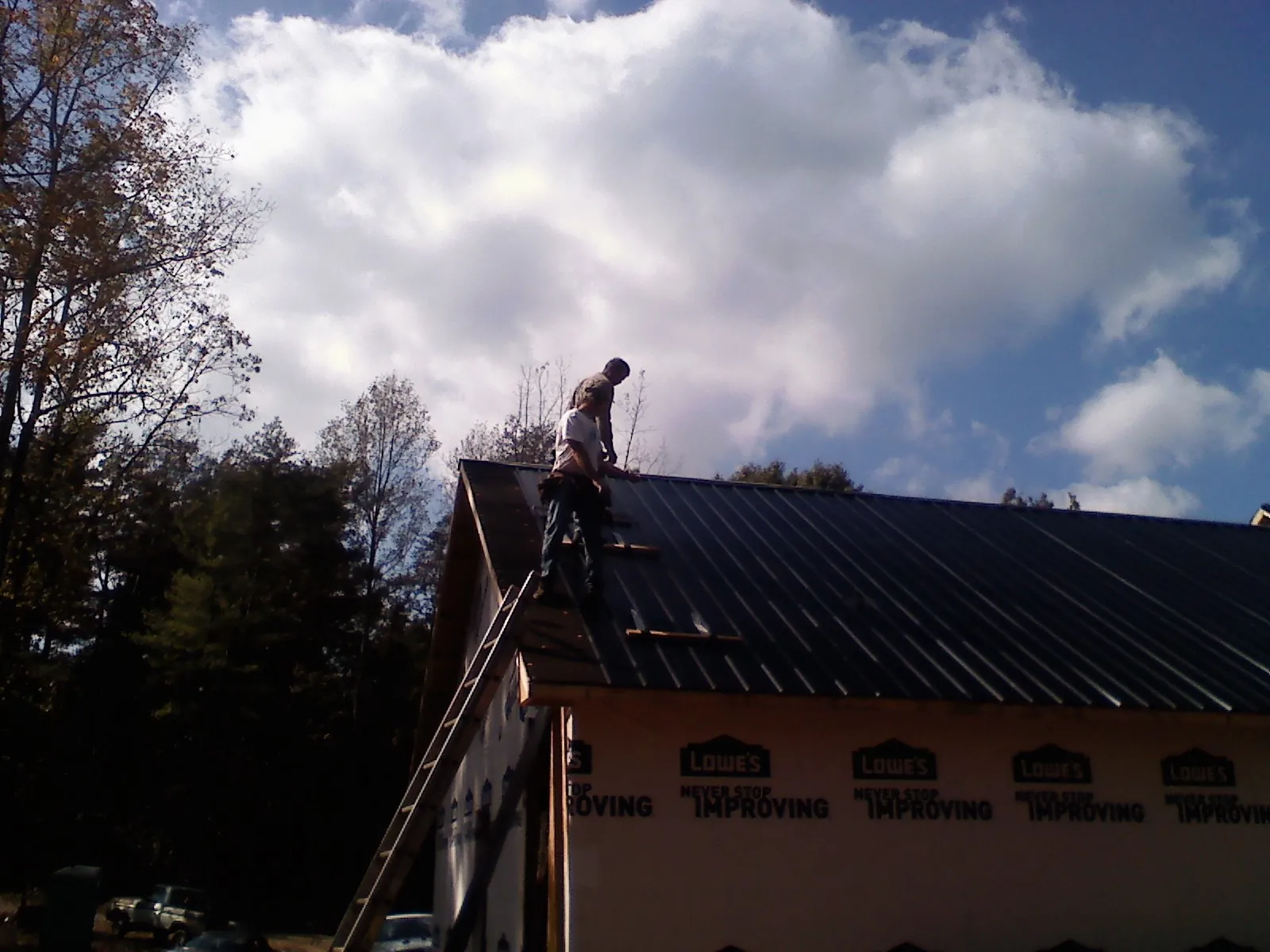 Roofer fastening dark metal panels high against a cloudy sky, from a Roof Inspection job in Okemos