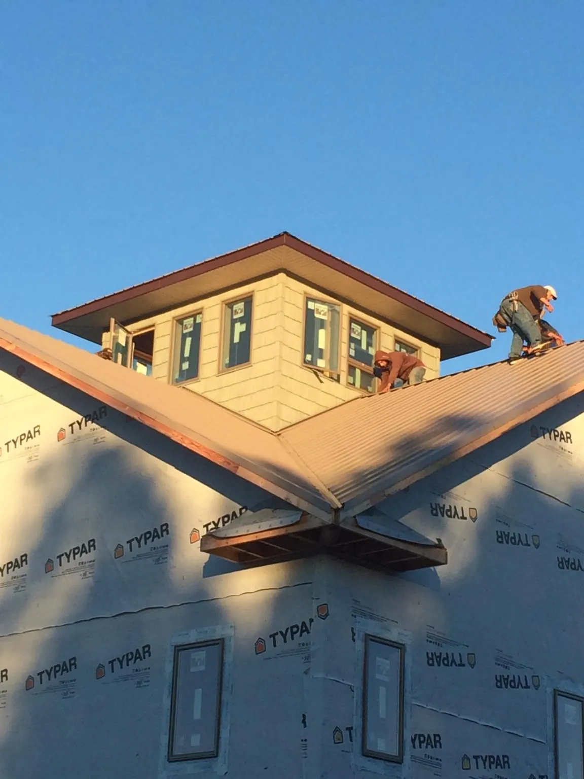 Roofers working around a rooftop cupola on a new metal roof at sunset — Roof Waterproofing in Okemos by Roofing Brothers
